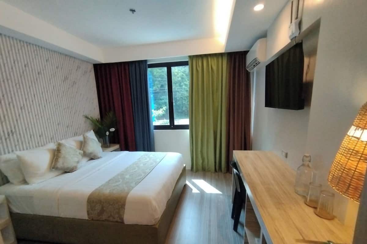 Habitación de hotel moderna con cama, escritorio, televisor y ventana con cortinas.