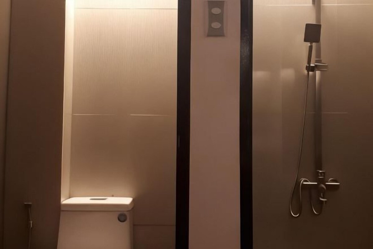 Une salle de bain équipée de toilettes, d’une douche et d’un panneau de commande fixé au mur.