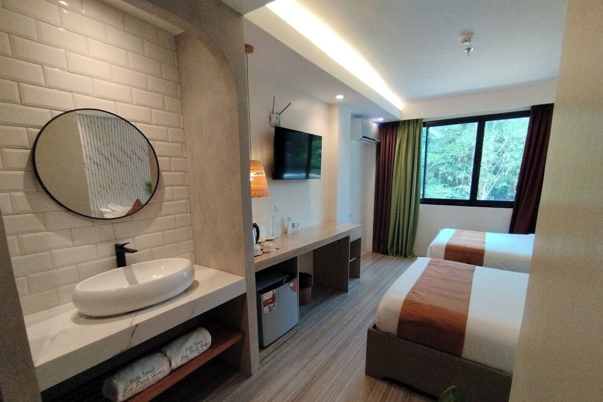 Habitación de hotel con baño, cama, televisión y ventana con cortinas.