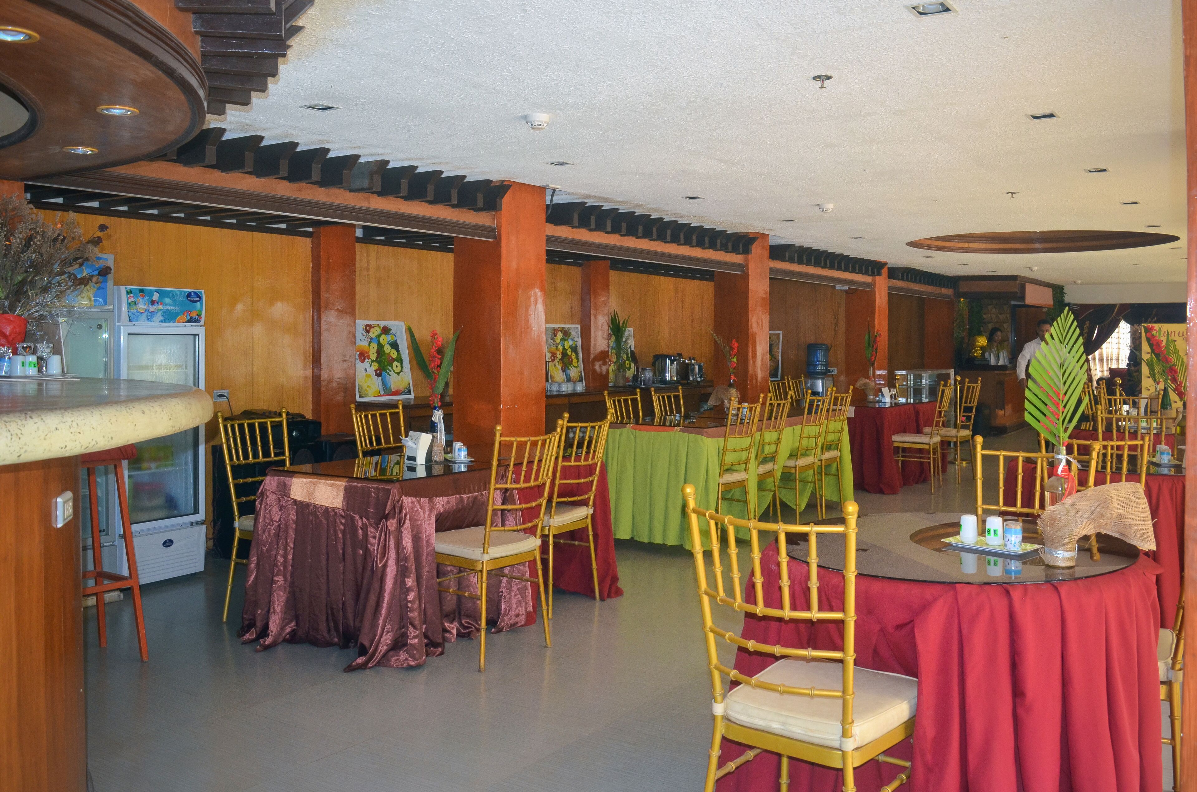 Un restaurant amb diverses taules i cadires, panells de fusta i una barra amb una caixa registradora.
