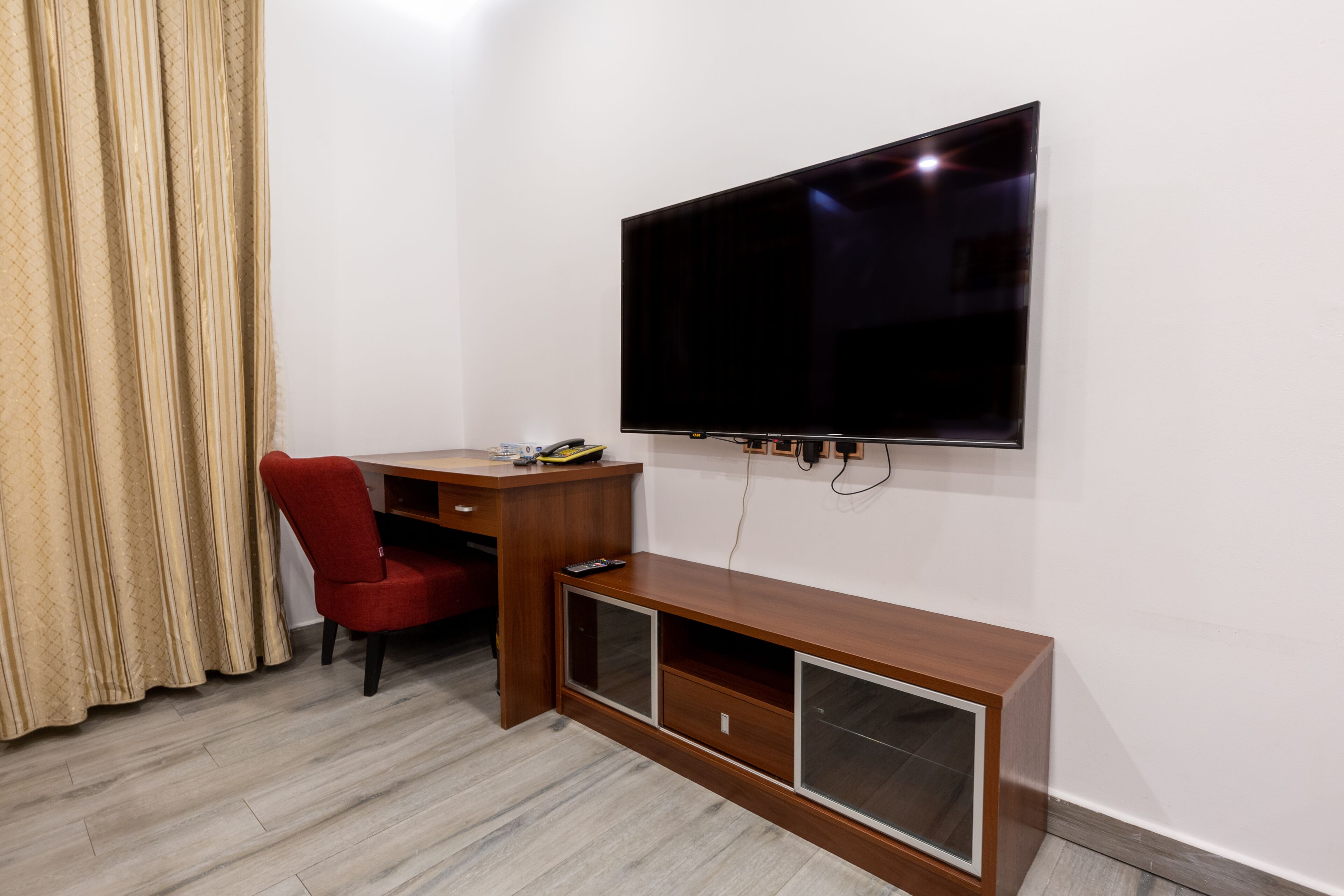 A room with a flat-screen TV mounted on the wall, a wooden desk with a chair, and a built-in cabinet.