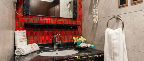Un baño con un lavabo de mármol negro, una pared de mosaico rojo, una toalla blanca y un secador de pelo en la pared.