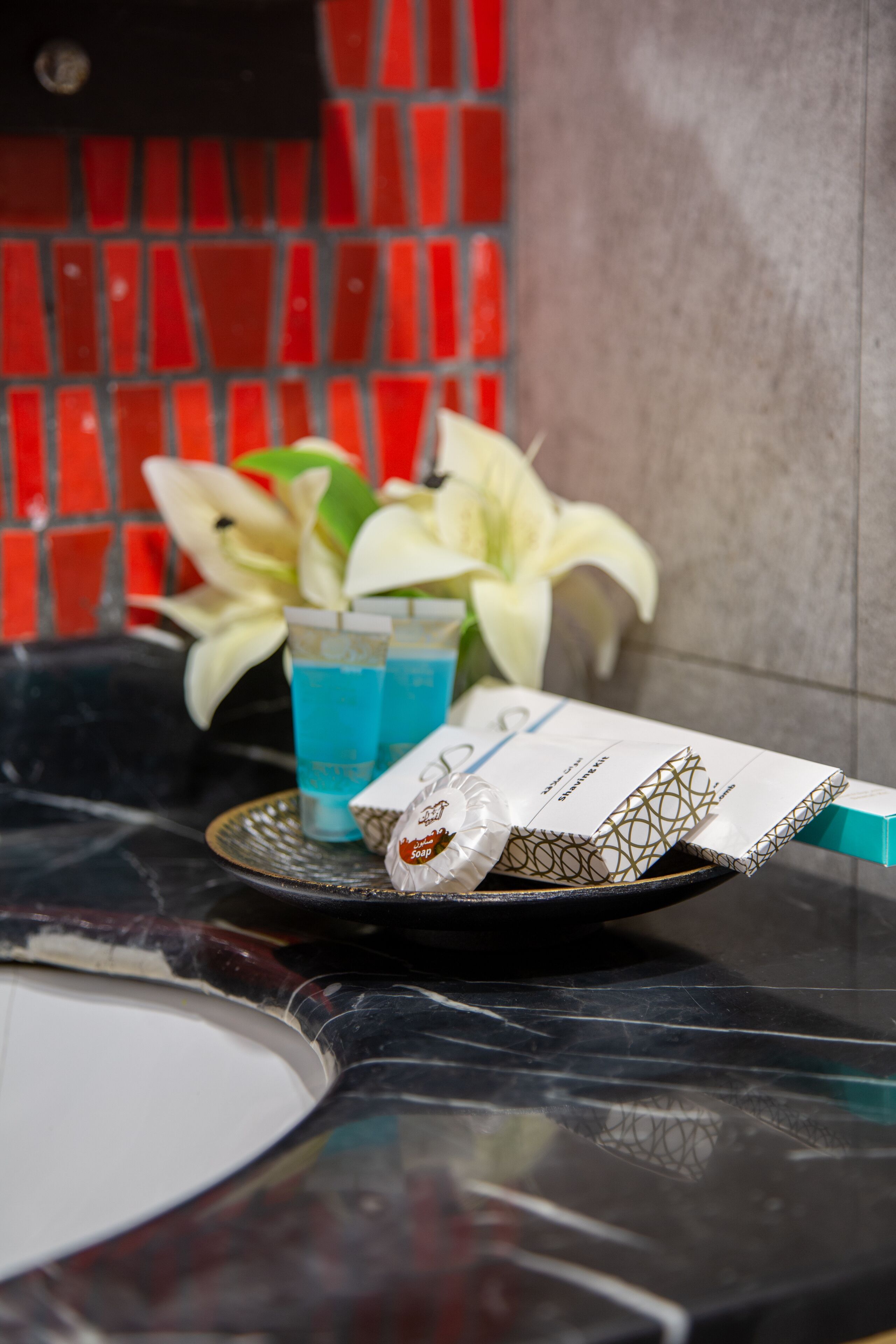 A bathroom with a black marble sink, a glass of blue liquid, a white towel, and a soap bar on a tray.