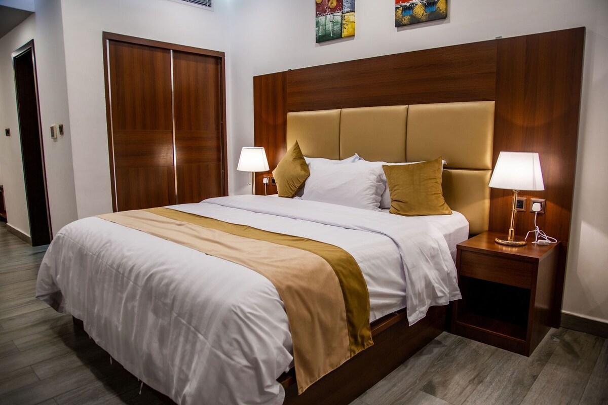 A hotel room with a large bed, wooden headboard, two bedside tables with lamps, and a door.