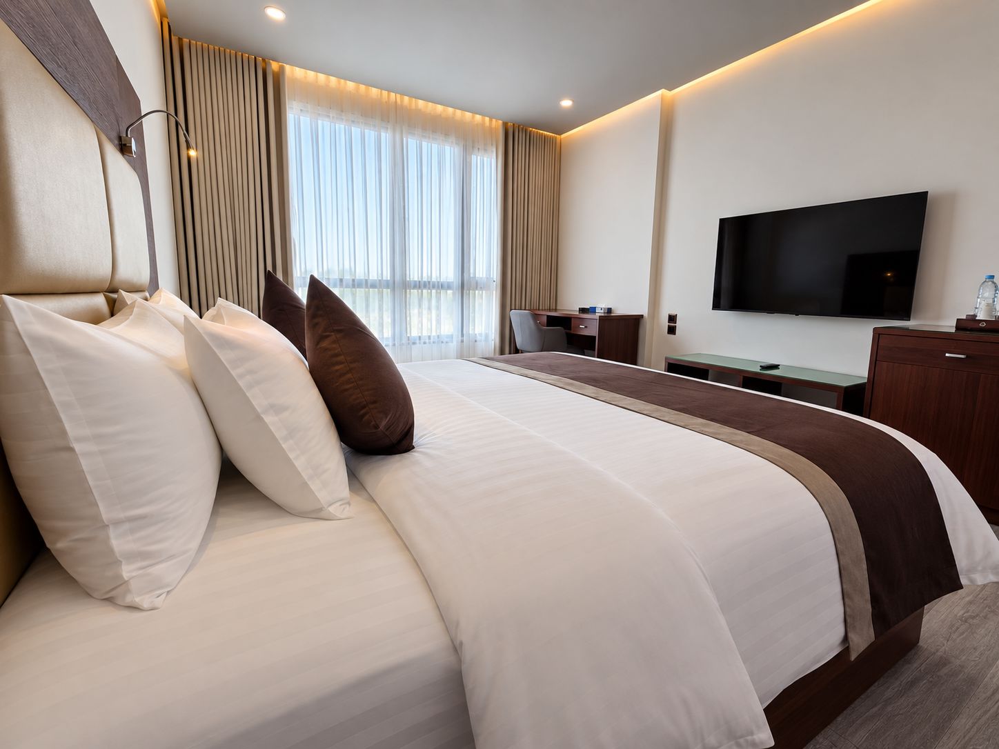 Habitación de hotel con una cama grande, un escritorio, un televisor de pantalla plana y un ventanal con cortinas.