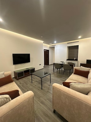 Una sala de estar moderna con un televisor de pantalla plana, una mesa de centro, sofás y un comedor con sillas.