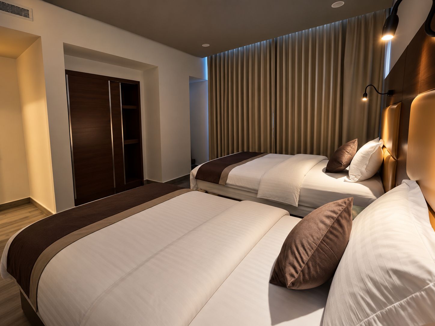 A hotel room with two beds, a wardrobe, and a curtain wall.