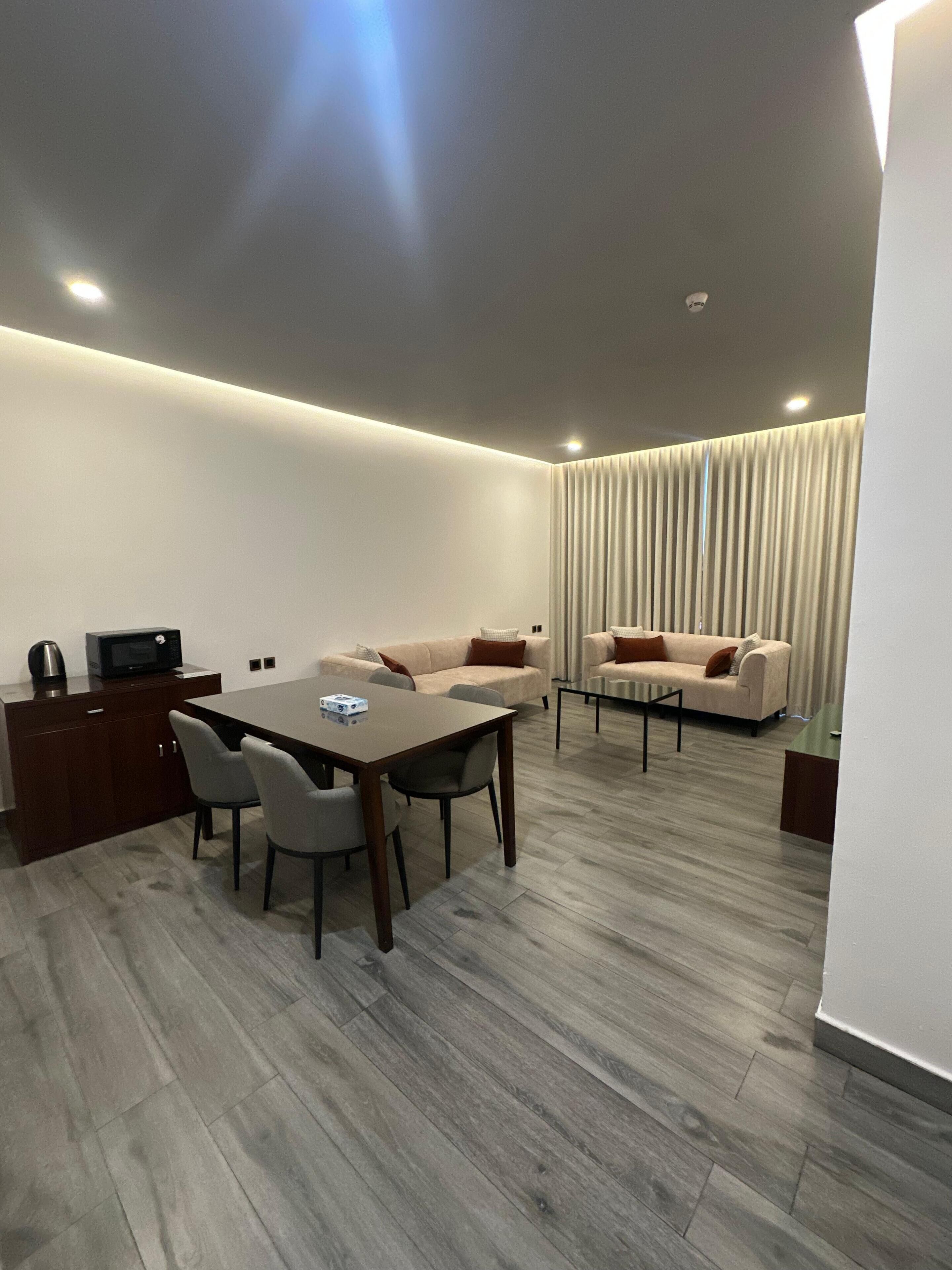 A modern hotel room with a dining area, a sofa set, and a kitchen area.
