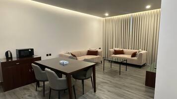 A modern hotel room with a dining area, a sofa set, and a kitchen area.