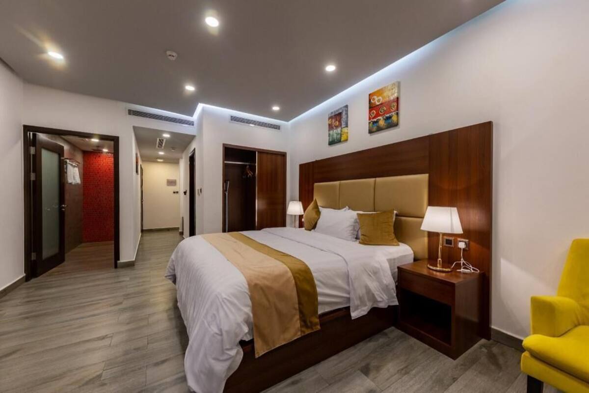 A hotel room with a large bed, bedside tables, a chair, and a red accent wall.