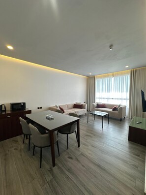 A modern living room with a dining table, two sofas, a coffee table, and a TV on a stand. - Rosalina Hotel (Yanbu)
