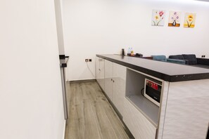 Una cocina moderna con suelo de madera, encimera negra y horno empotrado. Tres obras de arte enmarcadas adornan la pared sobre la encimera.