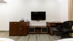 A hotel room with a wooden desk, a television mounted on the wall, a minibar, a trash can, and a black office chair. - Rosalina Hotel (Yanbu)