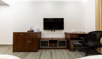 Habitación de hotel con escritorio de madera, televisor montado en la pared, minibar, cesto de basura y silla de oficina negra.
