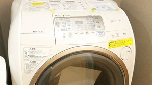 Eine Waschmaschine mit Frontöffnung, einer Bedienkonsole, einem Wasserzulauf und einem Ablaufschlauch.