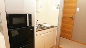 Eine kleine Küche mit einer schwarzen Mikrowelle und einem Kühlschrank, einem kleinen Spülbecken und Holzschränken.