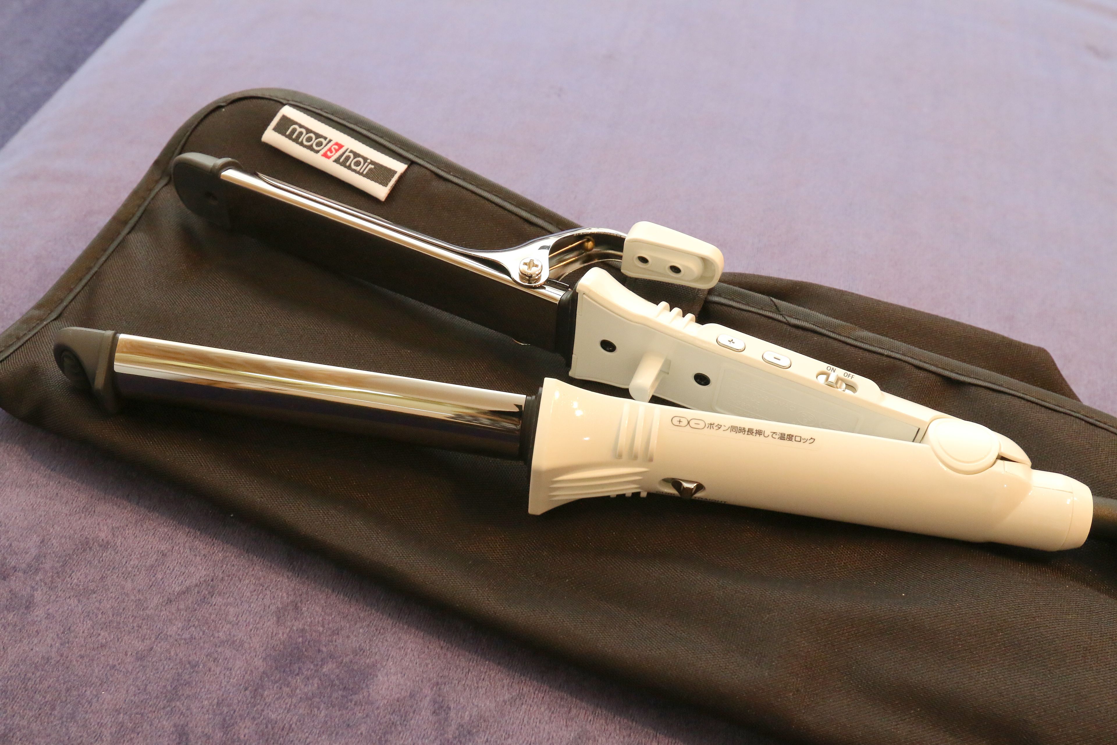 A hair styling tool in a brown case with a metal handle and a white plastic part.