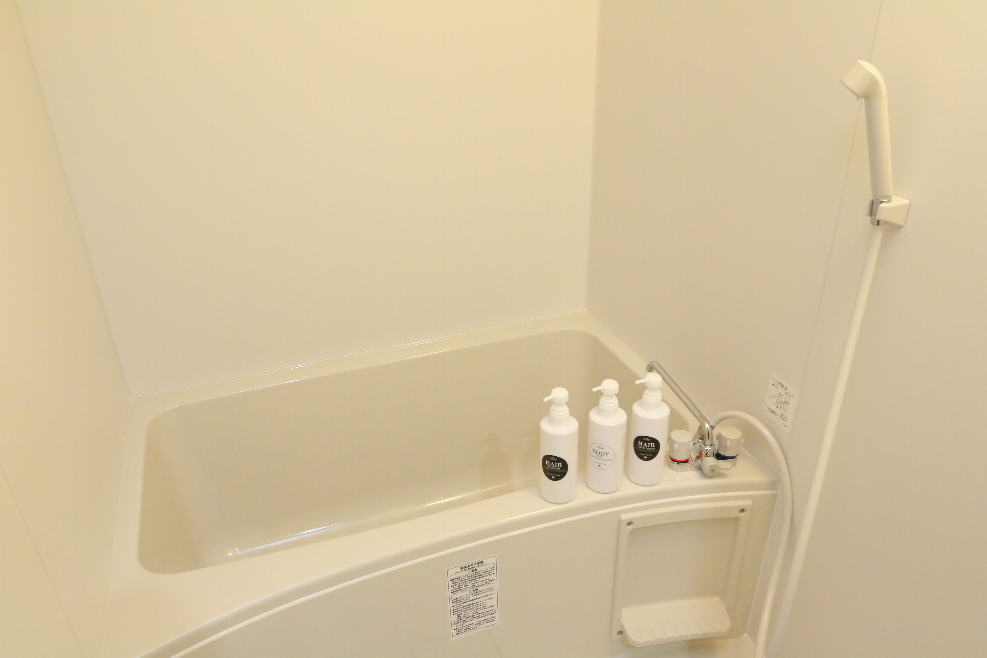 A bathroom with a bathtub, a shower, and three bottles of toiletries on the edge of the tub.