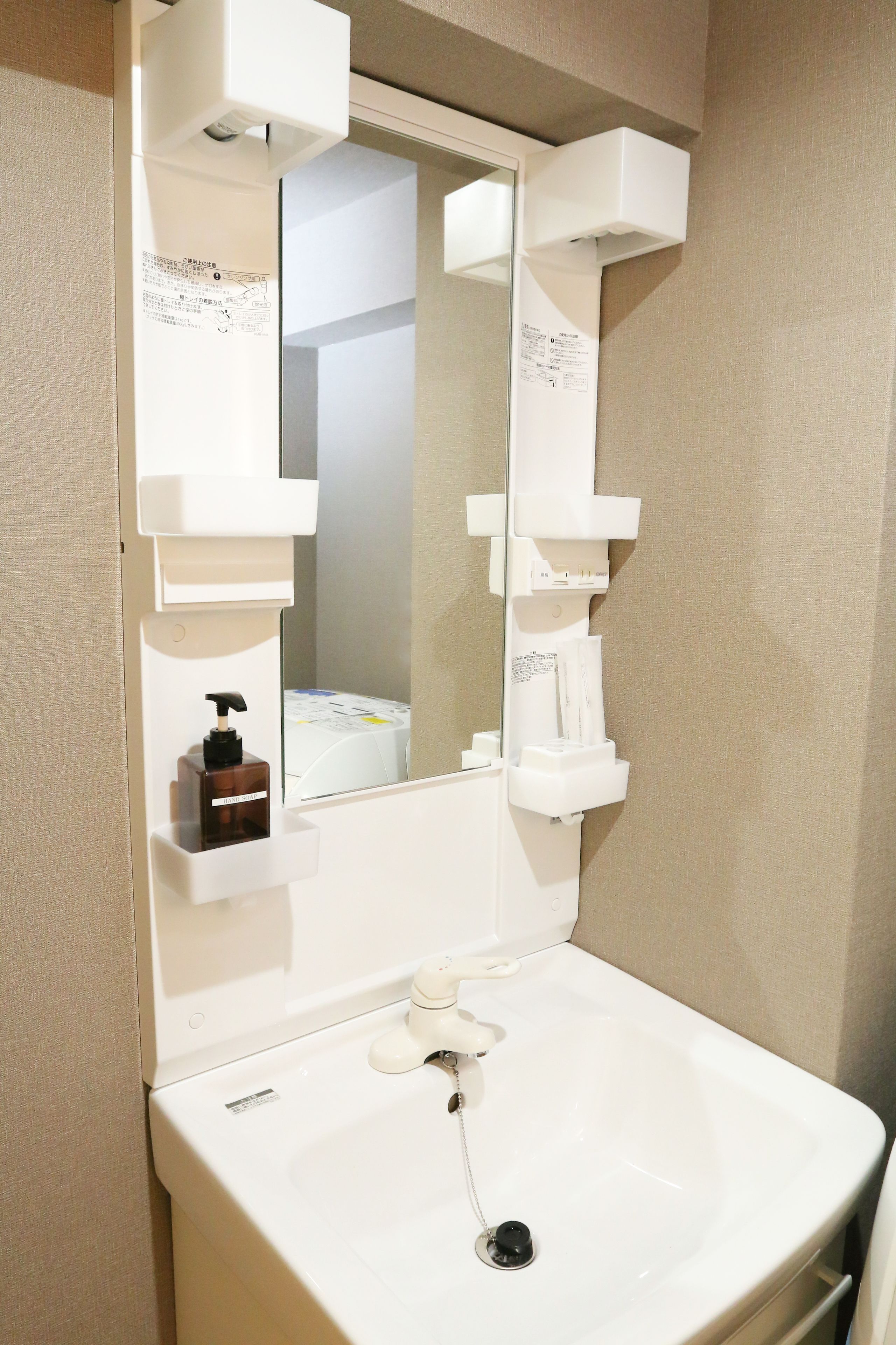 A bathroom with a white sink, a mirror, and a soap dispenser.