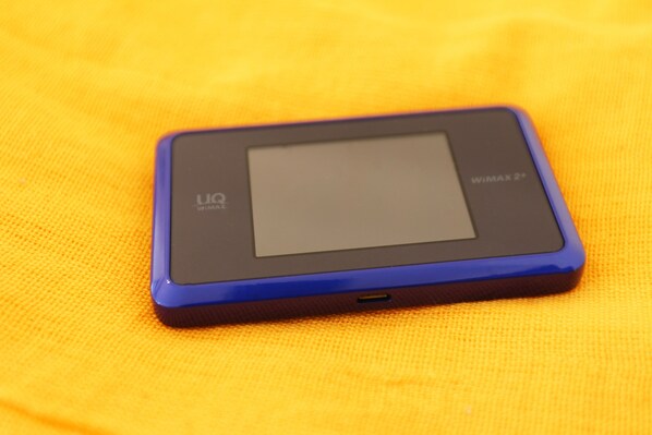 A small electronic device with a screen and buttons on a textured yellow surface.