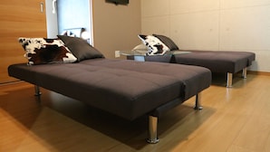 Ein modernes Zimmer mit zwei dunkelgrauen Betten, einem Glastisch und einem an der Wand befestigten Flachbildfernseher.