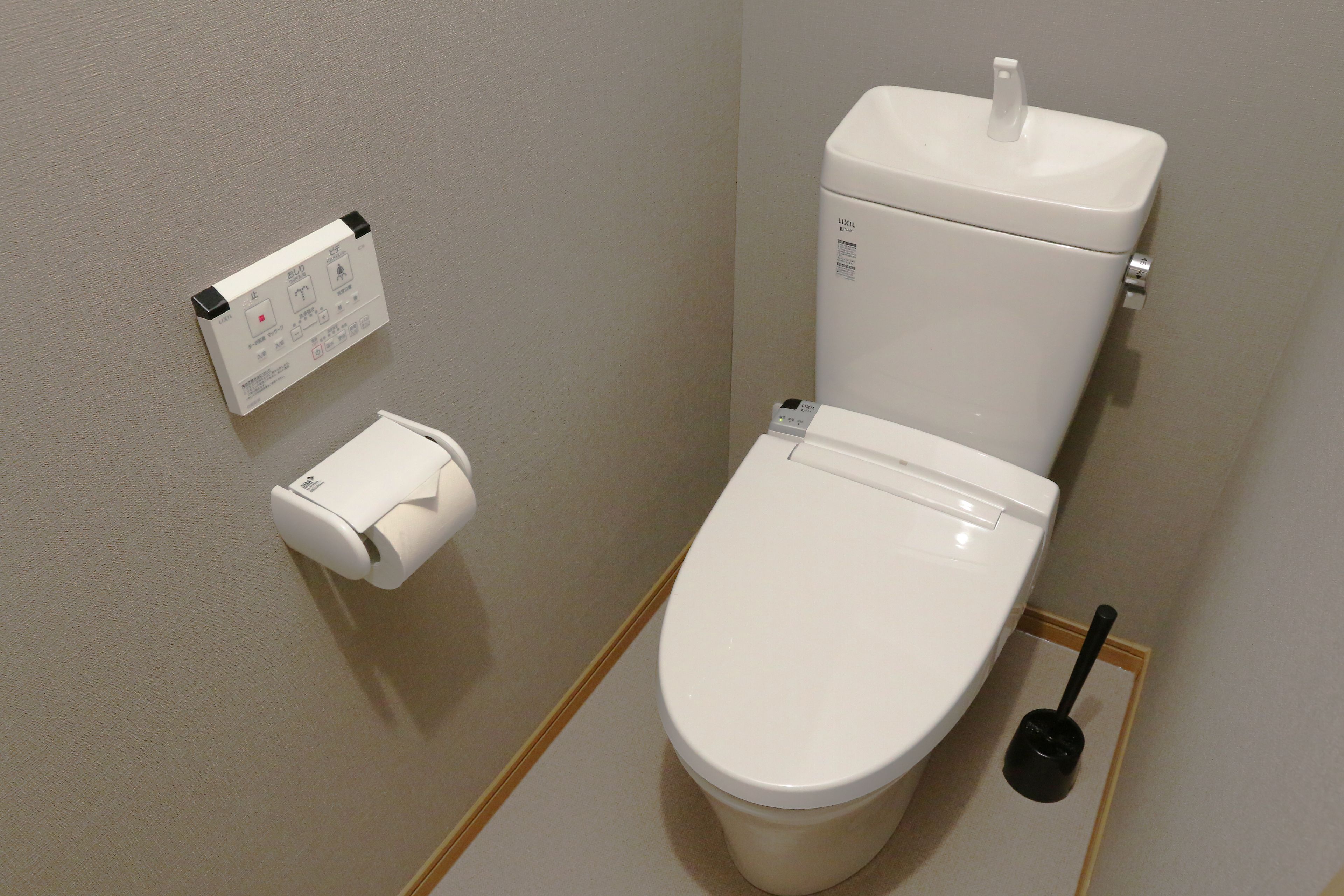 A white toilet with a flush handle and a plunger to the right.