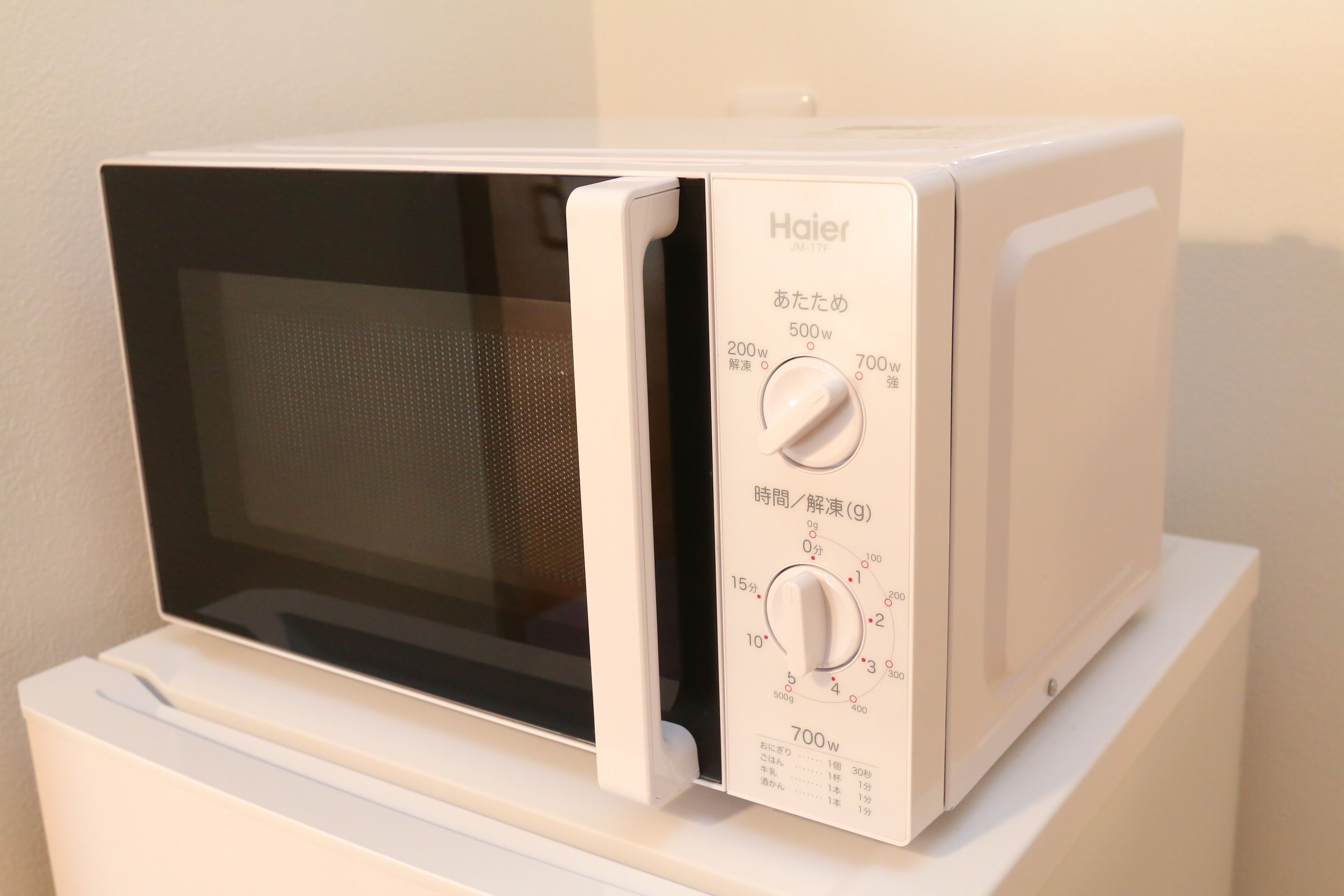 A white Haier microwave oven with two control knobs and a digital display, placed on a white countertop.