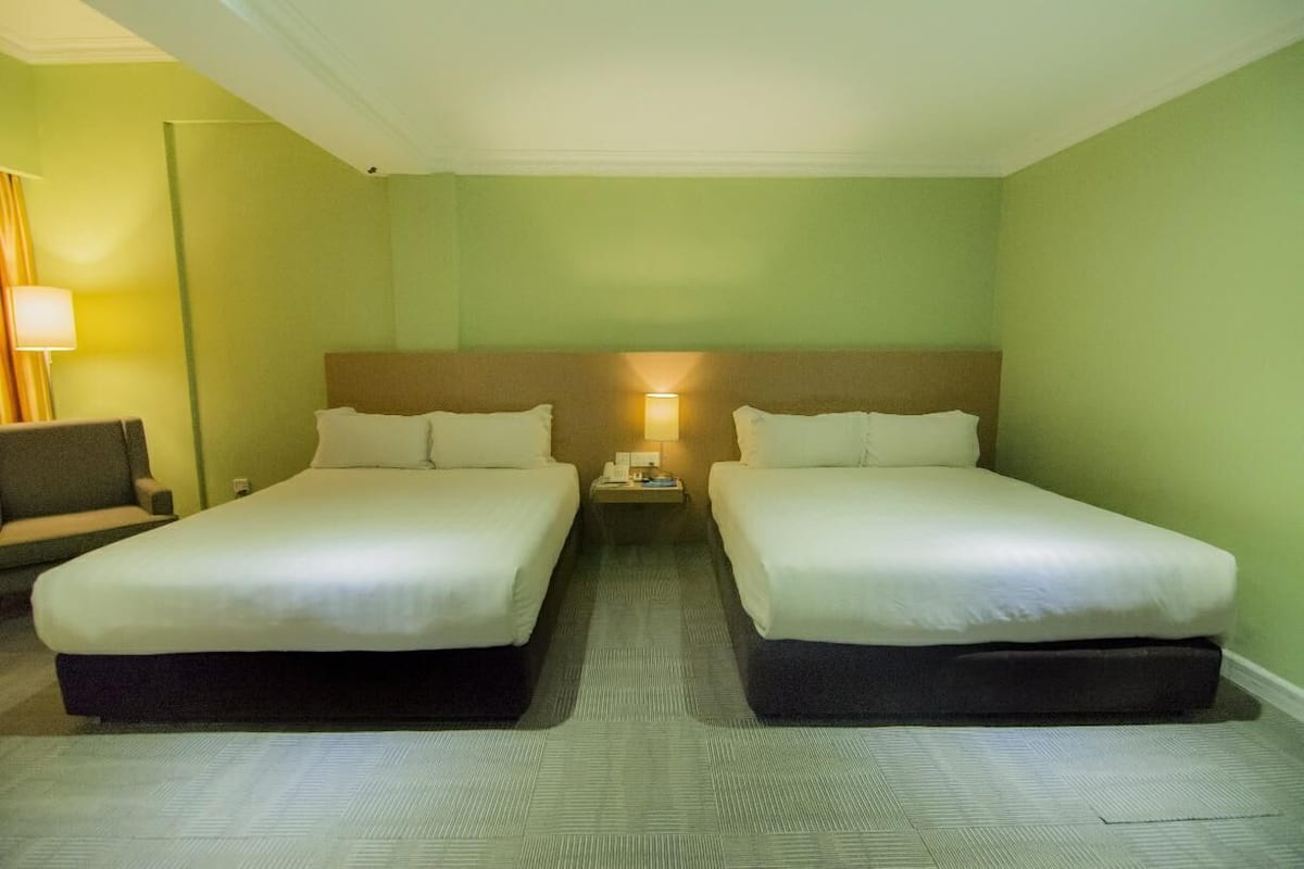 A hotel room with two beds, a nightstand, a lamp, and a chair.