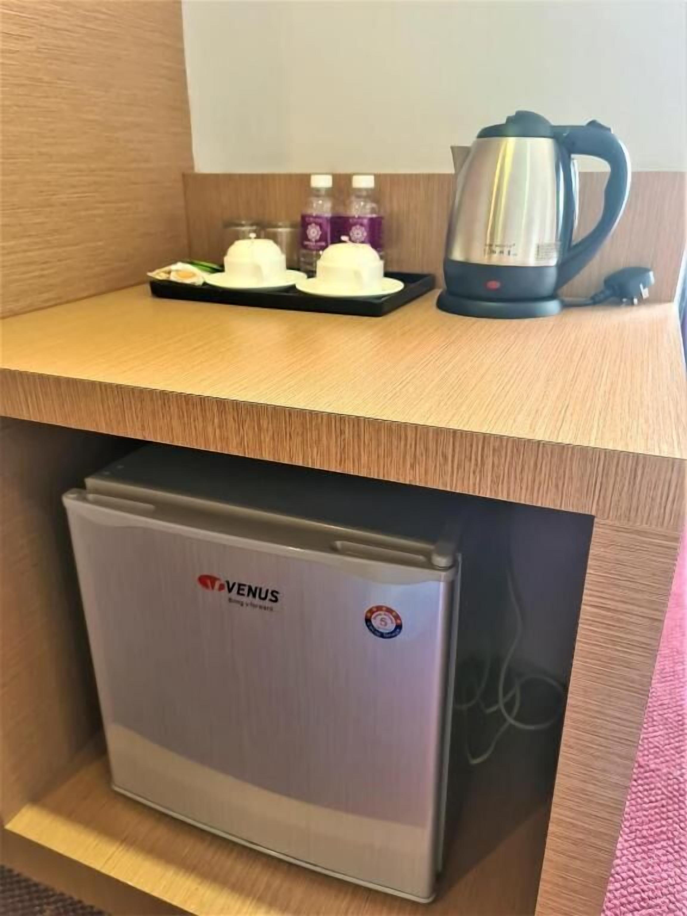 A compact kitchenette with a VENUS refrigerator, a coffee maker, and two bottles of water on the countertop.
