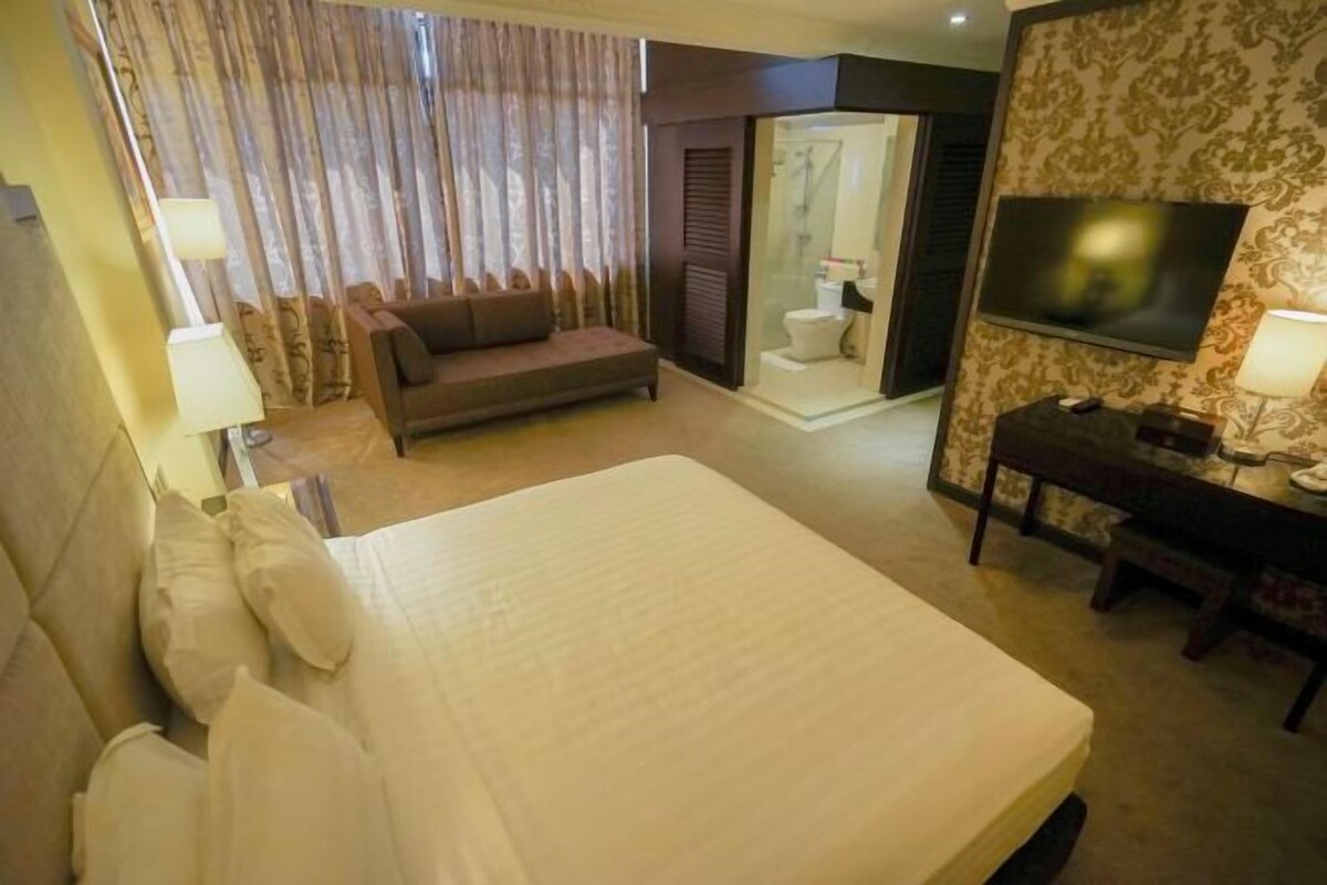 Habitación de hotel con una cama grande, un sofá, un escritorio, un televisor y una zona de ducha.