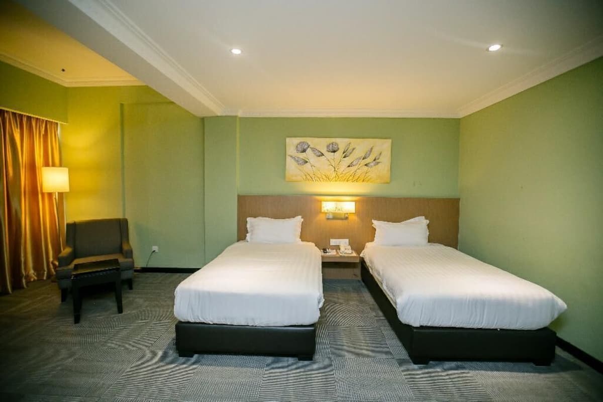 A hotel room with two beds, a desk, a chair, a lamp, and a painting on the wall.