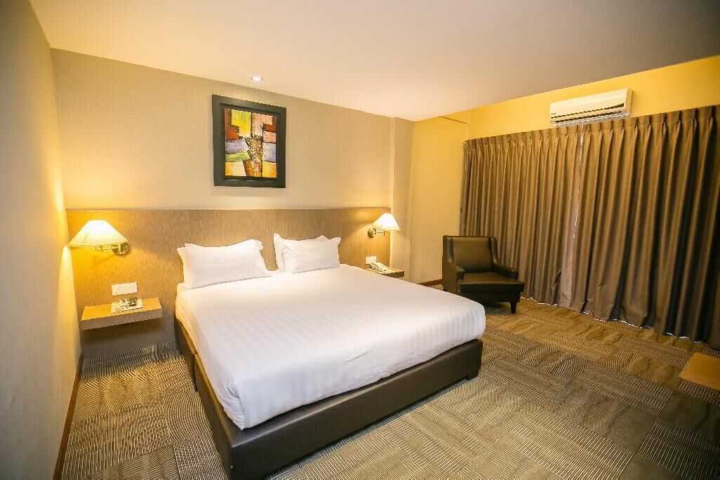 Habitación de hotel con una cama grande, dos lámparas de noche, una mesita, una silla, aire acondicionado de pared y un cuadro sobre la cama.