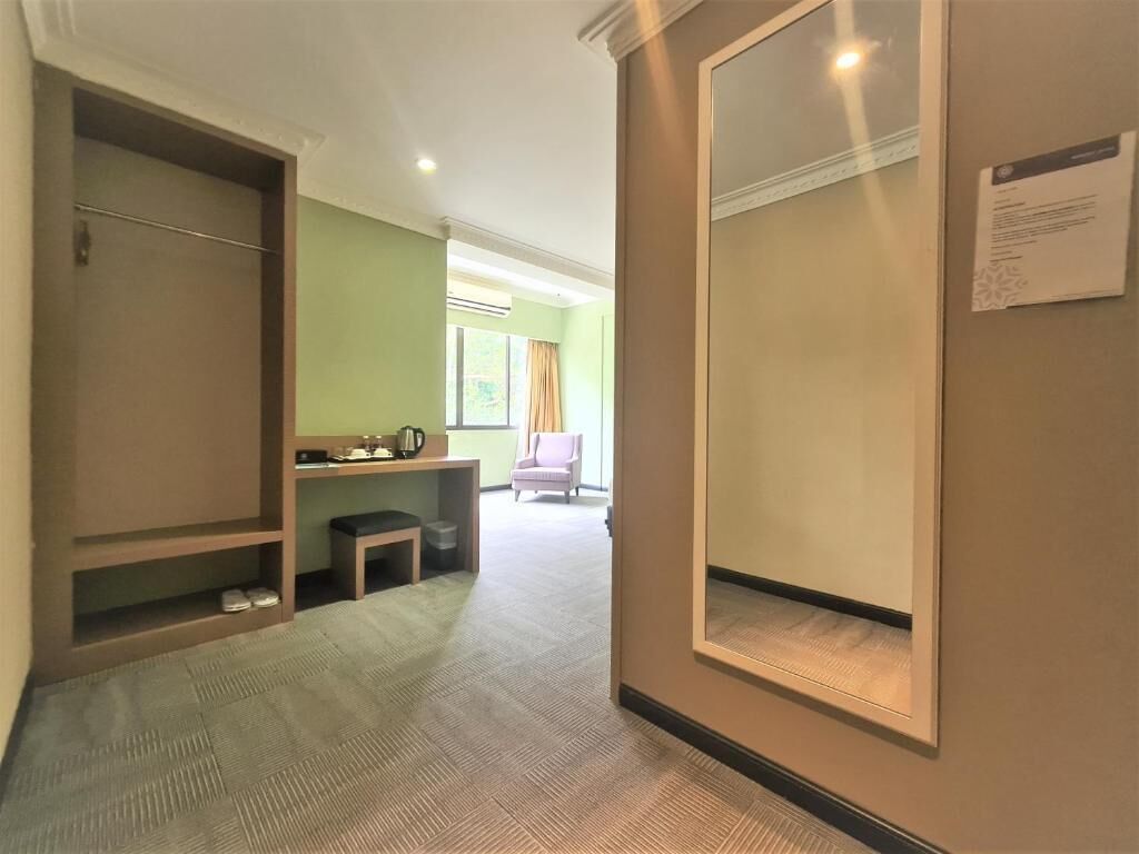 A hotel room with a large wardrobe, a small desk with a chair, and a window with curtains.