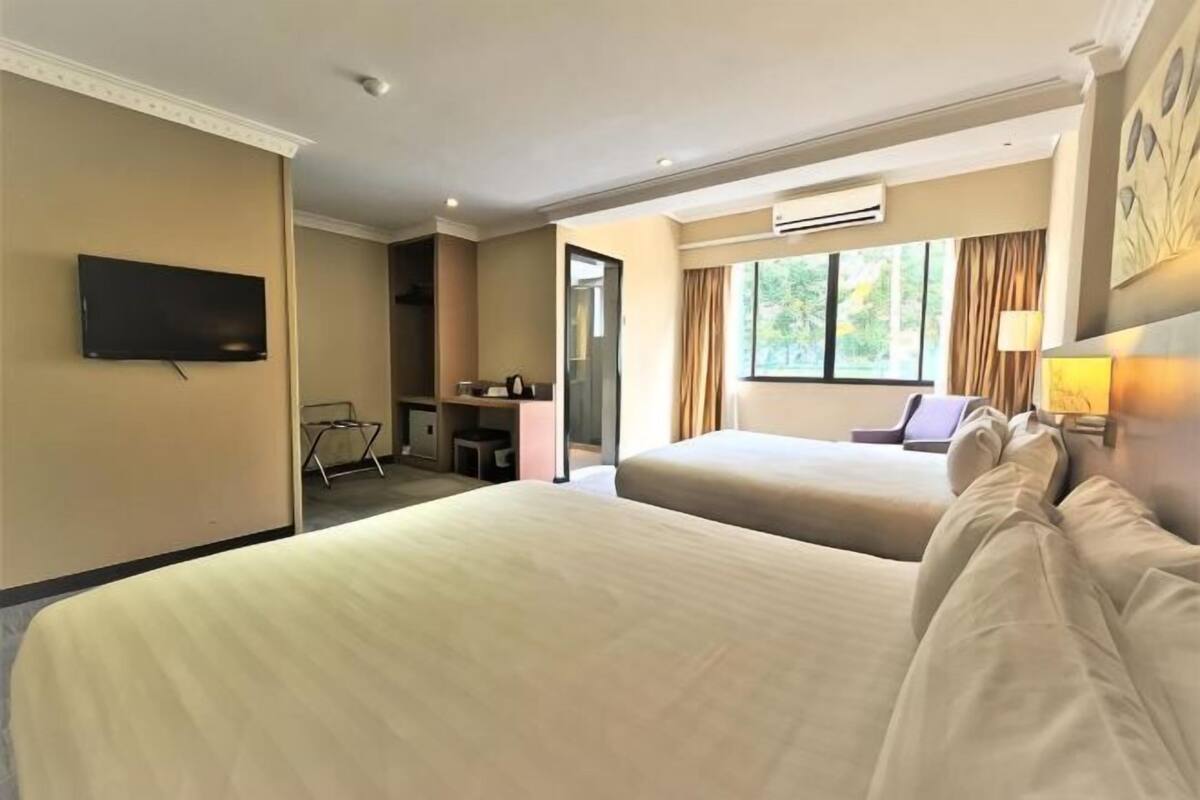 A hotel room with two beds, a desk, a TV, and a window with curtains.