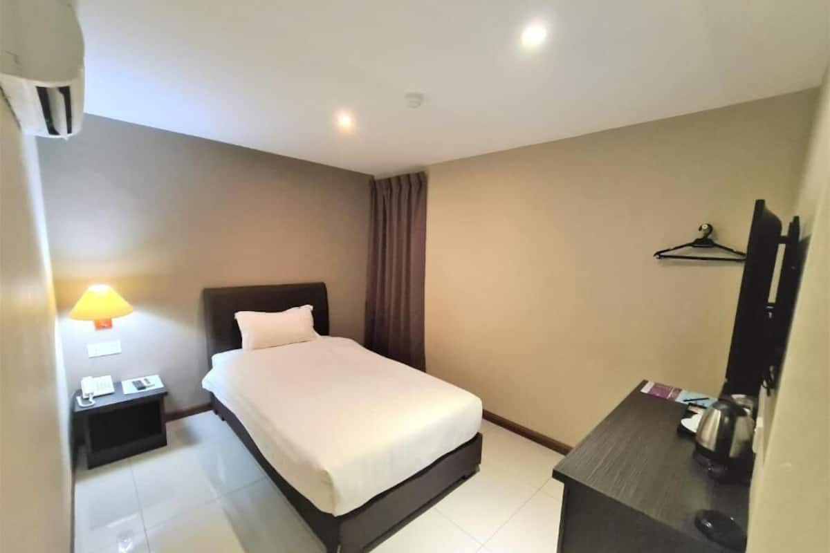 A hotel room with a bed, bedside table, lamp, and a desk with a chair.