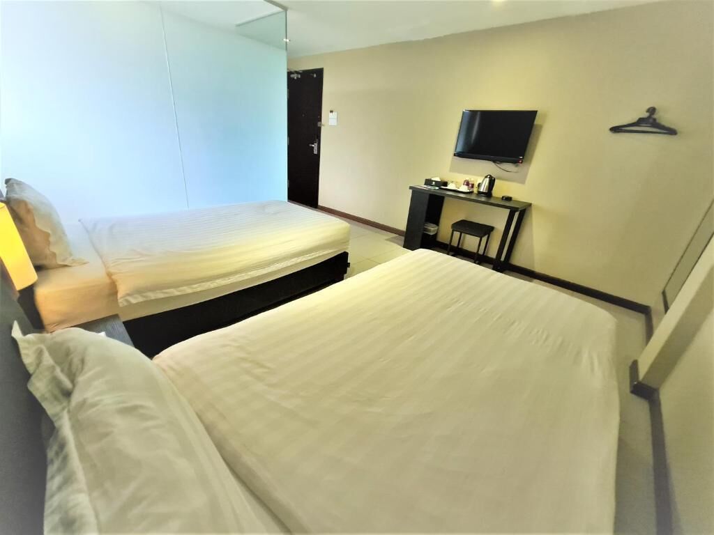 A hotel room with two beds, a desk, a chair, a TV, and a coat rack.