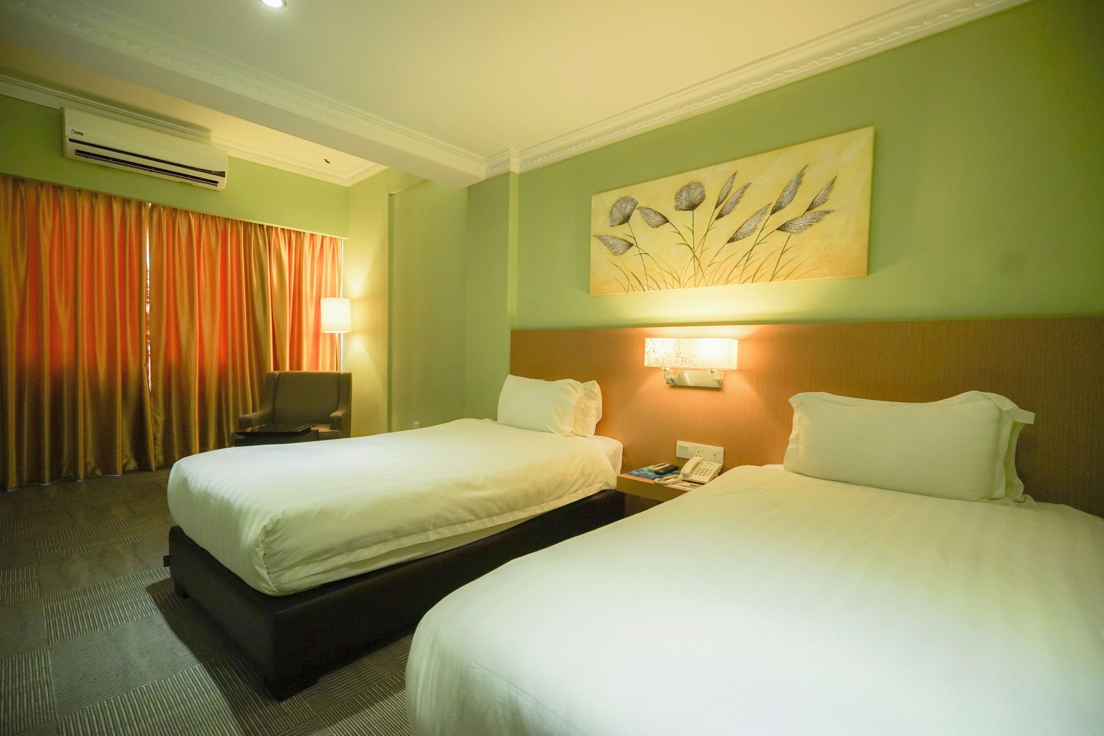 A hotel room with two beds, a desk, a chair, an air conditioner, and a painting on the wall.