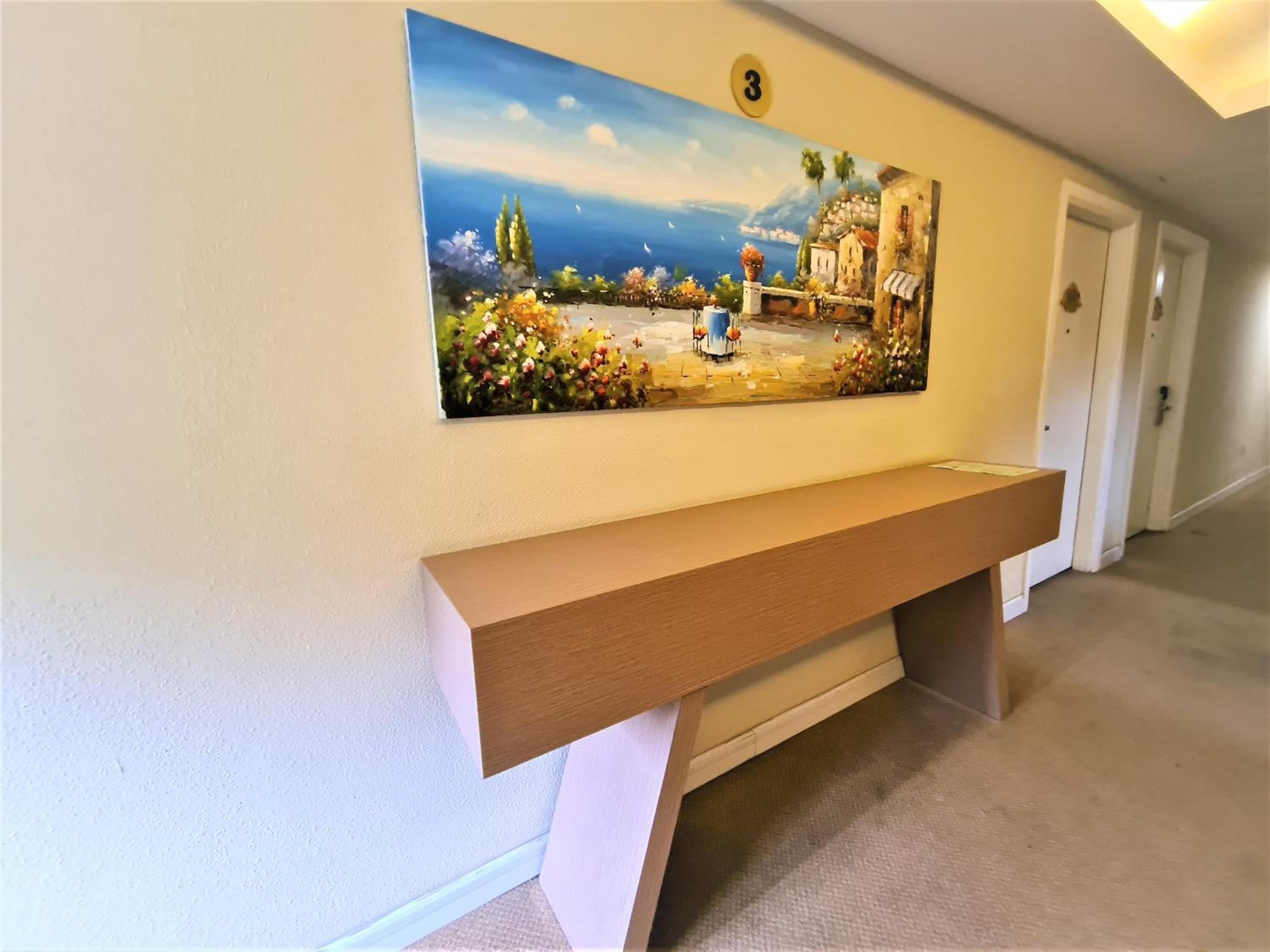 A hallway with a wooden bench, a painting of a coastal scene, and a door.