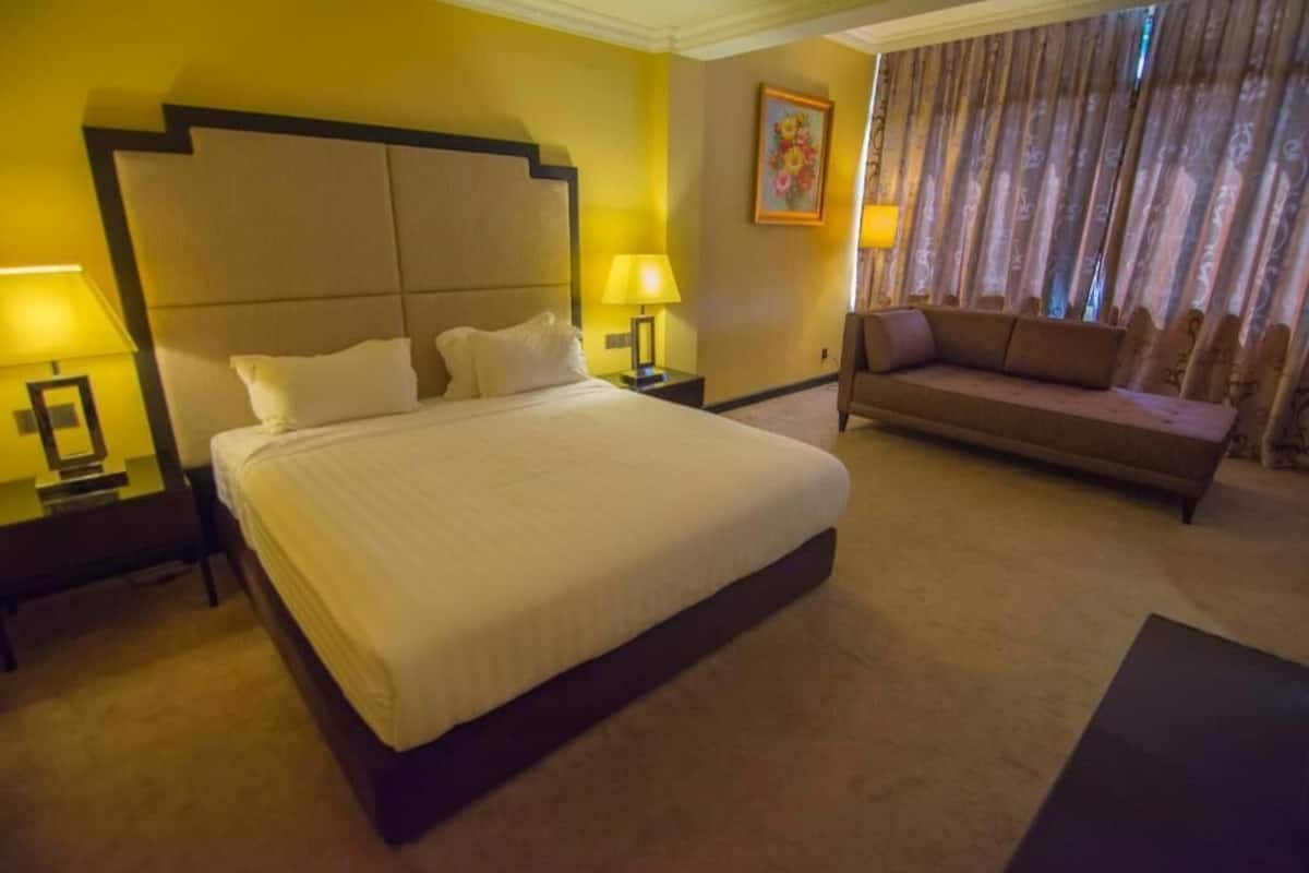 A hotel room with a large bed, two bedside tables with lamps, a sofa, and a curtain.
