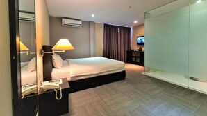 A modern hotel room with a large bed, bedside lamps, a flat-screen TV, a wardrobe, and a glass partition. - Merdeka Hotel (Kluang)