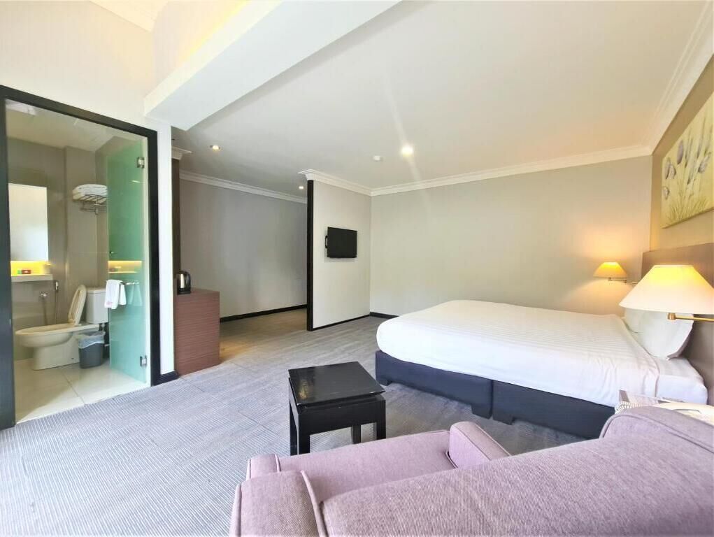 A hotel room with a bed, a sofa, a small table, a TV, and a bathroom visible through an open door.