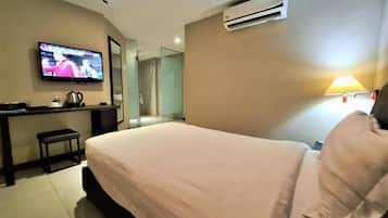 A hotel room with a bed, a TV mounted on the wall, a desk with a chair, and an air conditioning unit.