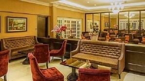 A lobby with a reception desk, red upholstered chairs, a large sofa, and framed artwork on the walls. - Merdeka Hotel (Kluang)