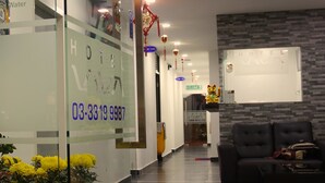 Un espace d’accueil d’hôtel avec une cloison en verre, un comptoir d’accueil, un canapé en cuir noir et un appareil de climatisation fixé au mur.