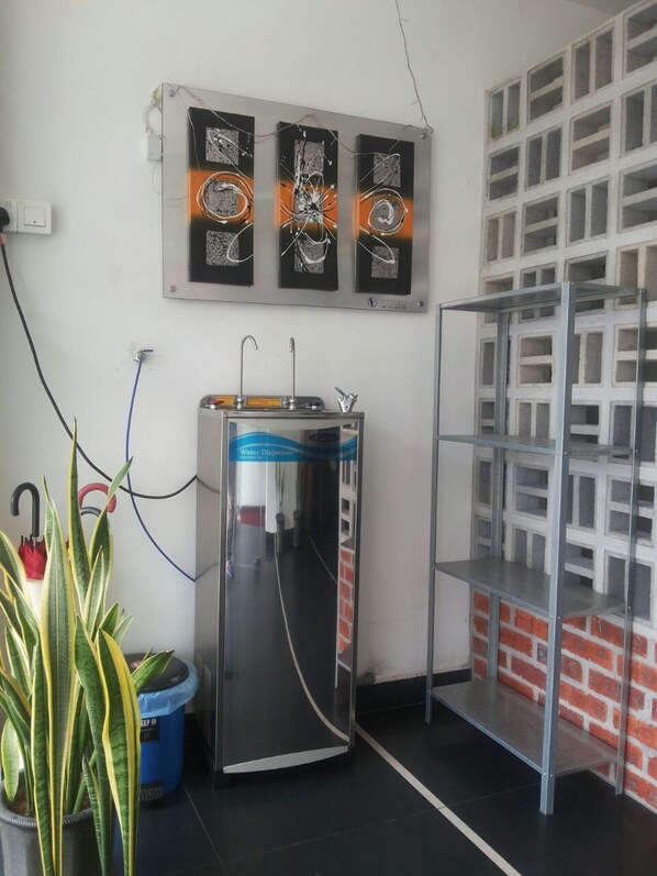 A room with a water dispenser, a potted plant, and a metal shelving unit. - Hotel Viva (Klang)