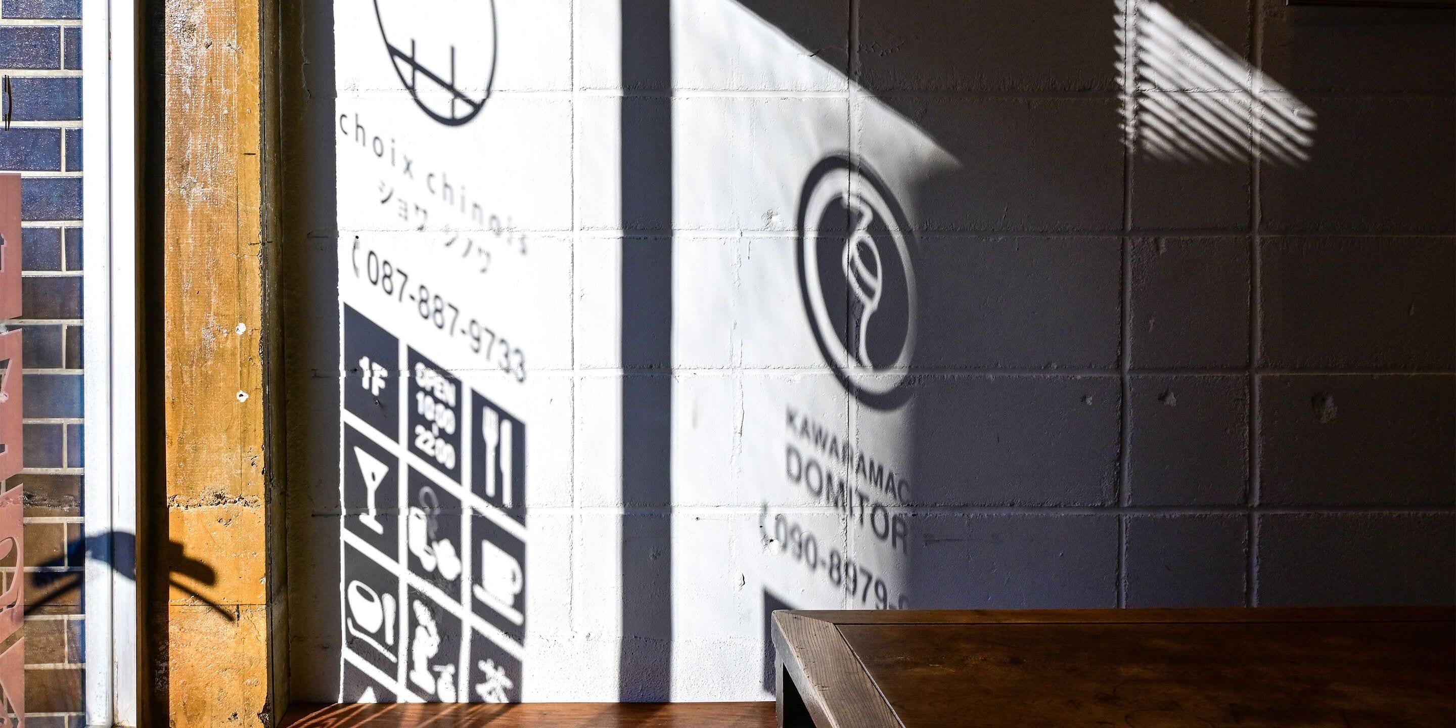 Een muur met een contactnummer en een logo, een houten bank en een bakstenen muur op de achtergrond.