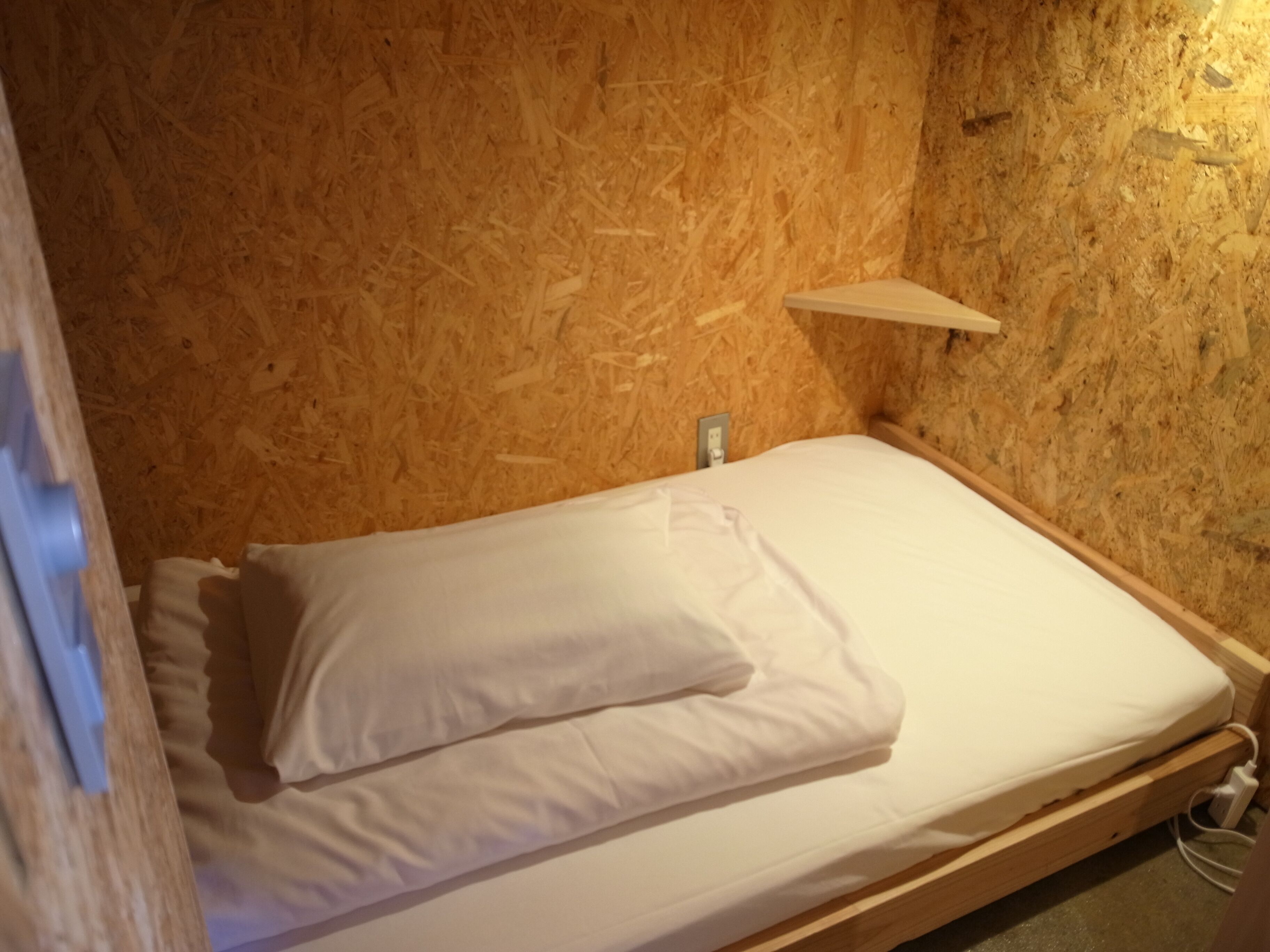 Ein Einzelbett mit weißer Bettwäsche in einem Zimmer mit Holzwänden und einem kleinen Regal.