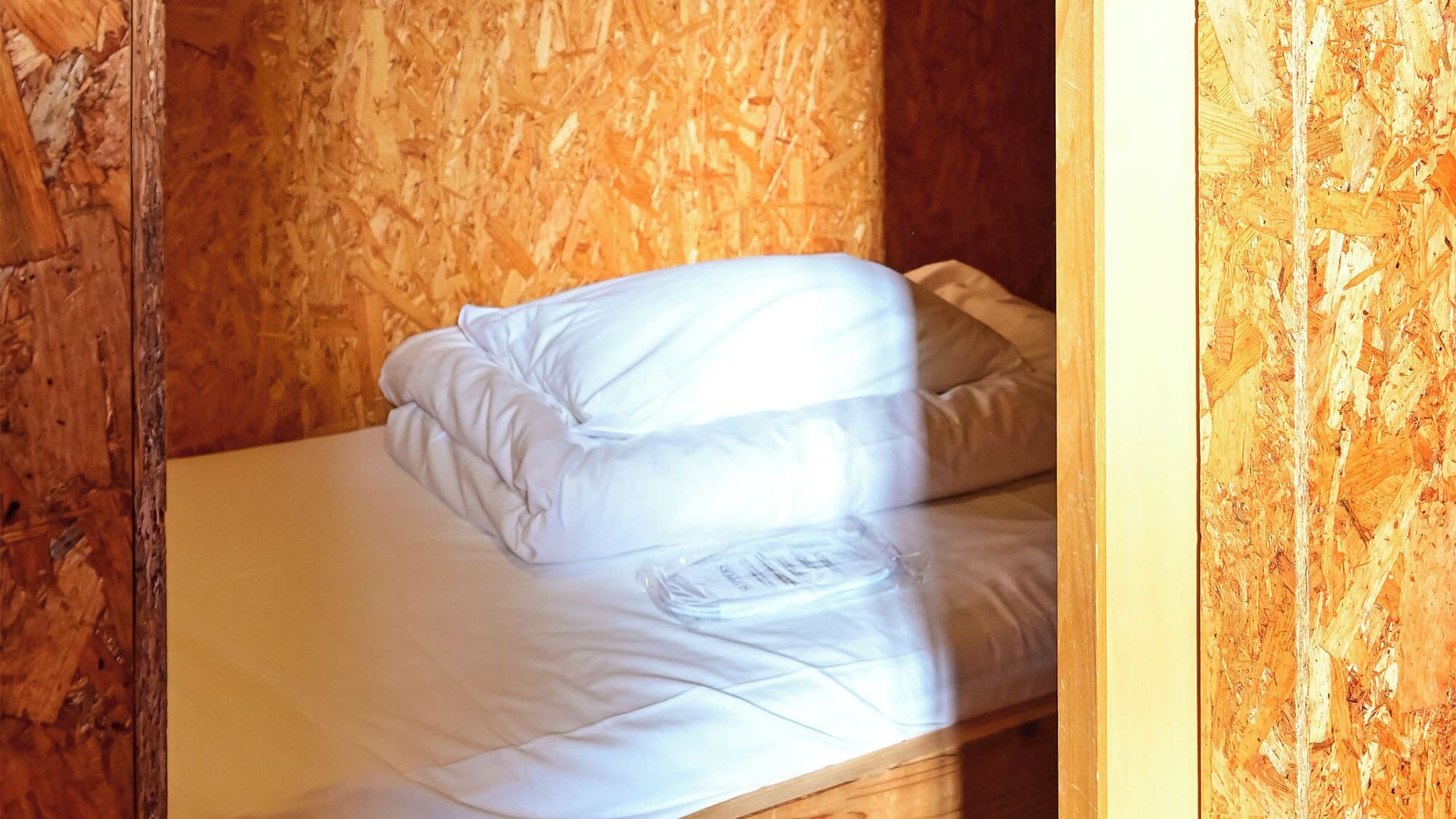 Ein Einzelbett mit weißer Bettwäsche in einem Raum mit Holzwänden.