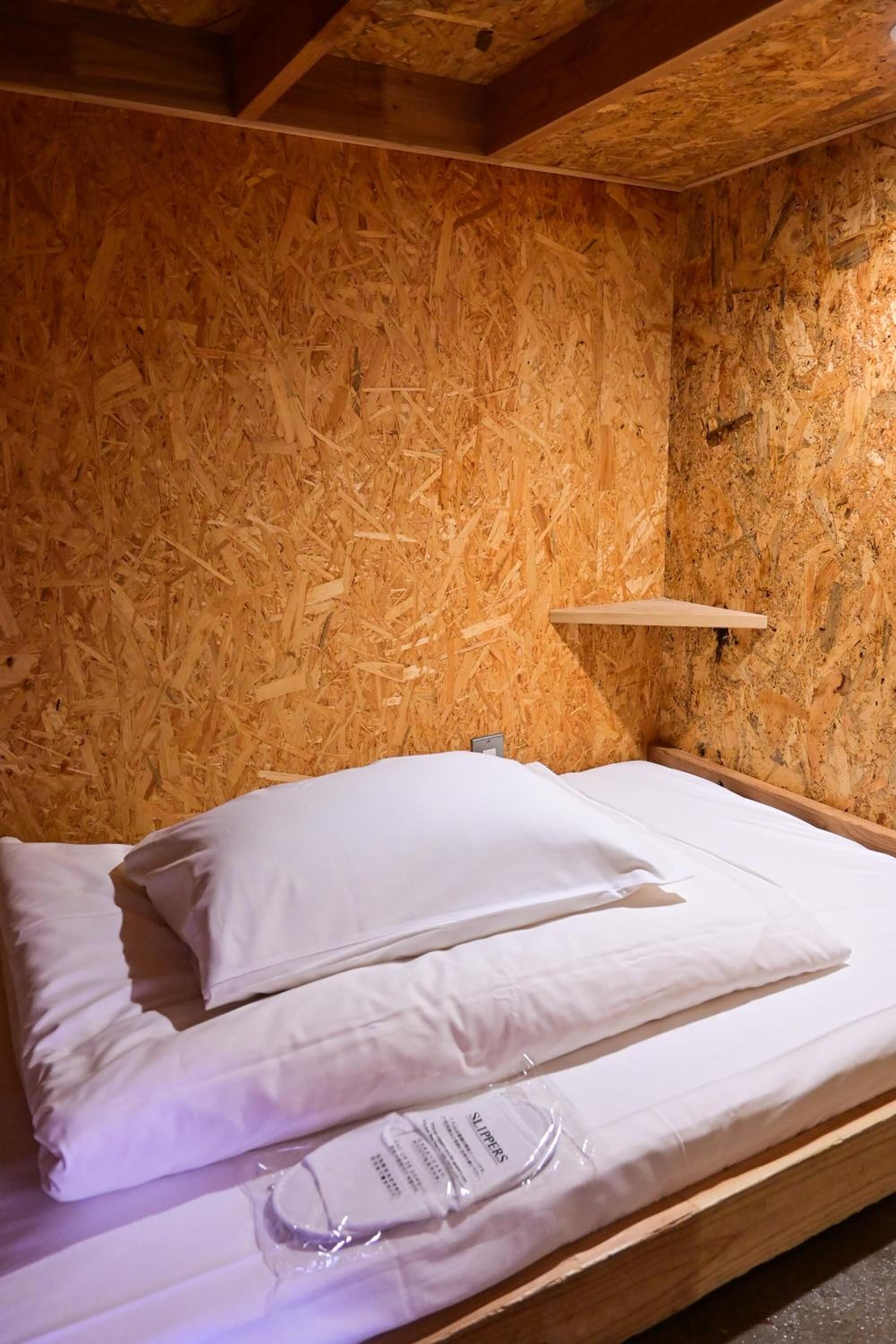 Een kamer met houten lambrisering, een bed, kussens en een klein plankje.