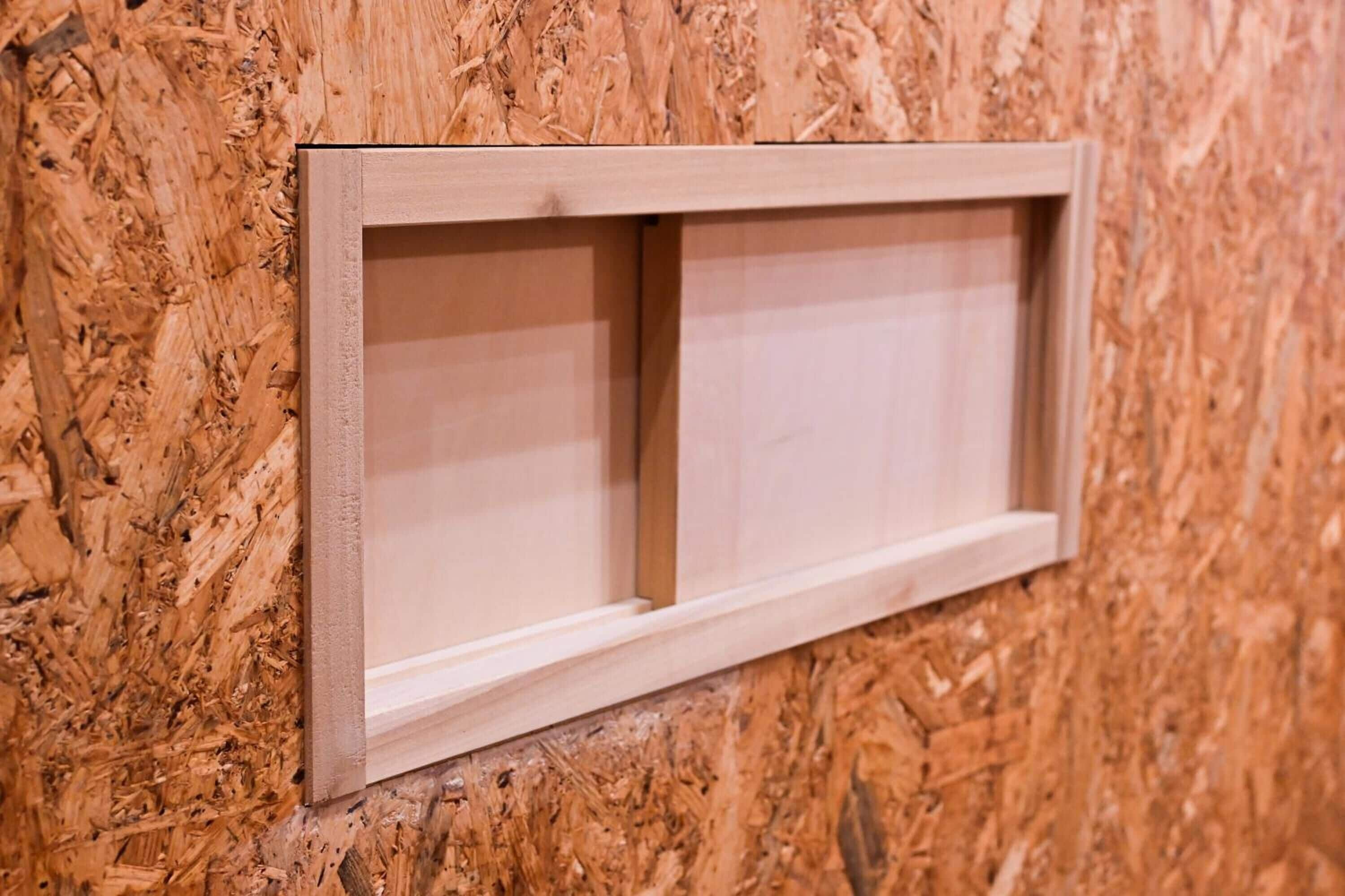 A wooden-framed window with a clear view of the interior wall.